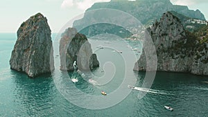 The Faraglioni rocks of Capri stand majestically under a clear sky. Gentle waves lap at the base of these natural