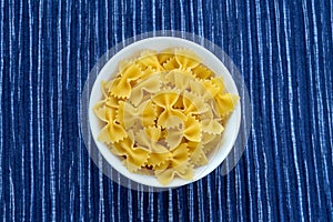 Farfalle macaroni Pasta in a white cup on a striped white blue cloth background in the center. Close-up with the top.