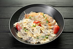 Farfalle with mushrooms, chicken fillet and parmesan in cream sauce in a black plate on the wooden table. Traditional