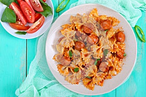 Farfalle pasta with chunks of sausage in tomato sauce on a bright background