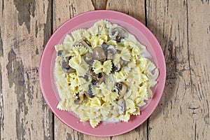 Farfalle pasta in a creamy sauce with champignon mushrooms in a plate on a wooden table.