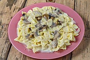 Farfalle pasta in a creamy sauce with mushrooms in a plate on a wooden table.