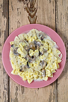 Farfalle pasta in a creamy sauce with mushrooms in a plate on a wooden table.