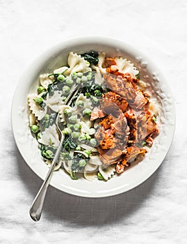Farfalle pasta with green peas spinach cream sauce and roasted salmon on light background, top view