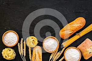 Farinaceous food. Fresh bread and raw pasta near flour in bowl and wheat ears on black background top view copy space photo