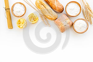 Farinaceous food. Fresh bread and raw pasta near flour in bowl and wheat ears on white background top view copy space