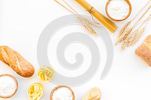 Farinaceous food. Fresh bread and raw pasta near flour in bowl and wheat ears on white background top view copy space