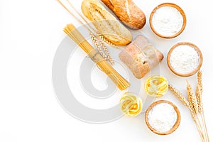 Farinaceous food. Fresh bread and raw pasta near flour in bowl and wheat ears on white background top view copy space