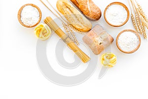 Farinaceous food. Fresh bread and raw pasta near flour in bowl and wheat ears on white background top view copy space