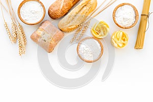 Farinaceous food. Fresh bread and raw pasta near flour in bowl and wheat ears on white background top view copy space