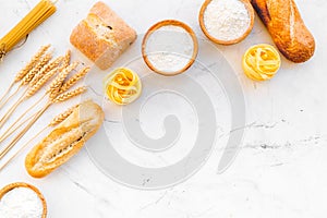 Farinaceous food. Fresh bread and raw pasta near flour in bowl and wheat ears on white stone background top view copy photo