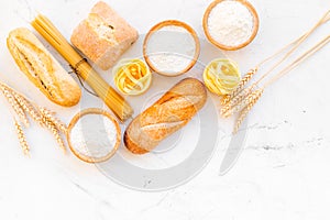 Farinaceous food. Fresh bread and raw pasta near flour in bowl and wheat ears on white stone background top view copy photo