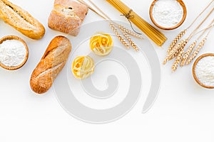 Farinaceous food. Fresh bread and raw pasta near flour in bowl and wheat ears on white background top view space for