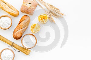 Farinaceous food. Fresh bread and raw pasta near flour in bowl and wheat ears on white background top view space for photo