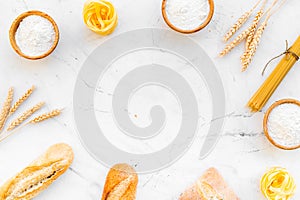 Farinaceous food. Fresh bread and raw pasta near flour in bowl and wheat ears on white stone background top view copy