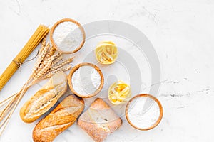 Farinaceous food. Fresh bread and raw pasta near flour in bowl and wheat ears on white stone background top view copy
