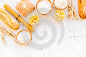 Farinaceous food. Fresh bread and raw pasta near flour in bowl and wheat ears on white stone background top view space