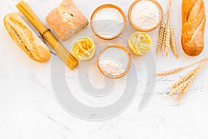 Farinaceous food. Fresh bread and raw pasta near flour in bowl and wheat ears on white stone background top view space