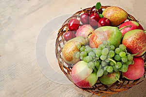 Farm apples, pears, grapes and plums in a wicker wooden plate on the table. Harvest of autumn fruits. Copy Space
