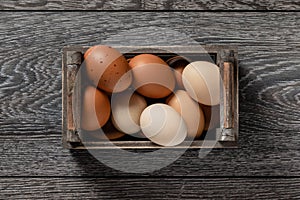 Farm fresh organic large brown and white eggs in crate on rustic dark oak wood background table.