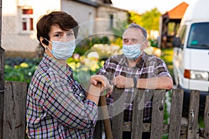 Farm neighbors in protective masks talk at the border of garden plot