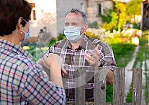 Farm neighbors in protective masks talk at the border of garden plot