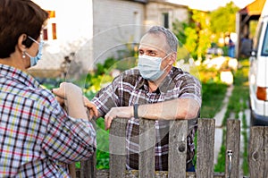 Farm neighbors in protective masks talk at the border of garden plot