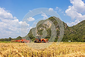 On a farm in Ratchaburi, Thailand, farmers use agricultural machine to compress and bundle rice straw