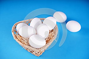 Farm raw, fresh white chicken egg in a basket on a blue background. Concept: a fresh egg for the morning breakfast