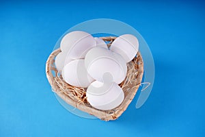 Farm raw, fresh white chicken egg in a basket on a blue background. Concept: a fresh egg for the morning breakfast