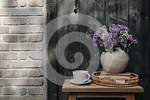 Farm spring breakfast still life. Purple, white lilac flowers bouquet in textured vase with cup of coffee. Wicker tray