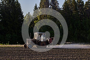 Farm tractor applies herbicides to potato crop using sprayer on boom. photo