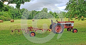 Farm tractor with attached hay rake in front of a recently-mowed field