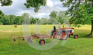 Farm tractor with attached hay rake in front of a recently-mowed field