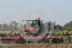 Farm Tractor in a farm field working in the field with dirt in the air and blue sky