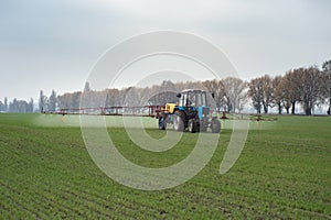 Farm tractor spraying agrochemical or agrichemical over young gr