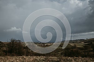 Farm of wind turbines for renewable wind energy on far horizon on hills of Romania under the dark cloudy sky. Copy space