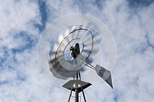 Farm windmill spinning on a sunny day with clouds