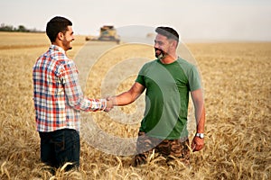 Farmer and agronomist shaking hands in wheat field after agreement. Agriculture business contract concept. Corporate