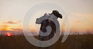 Farmer agronomist walking through ripe wheat field at sunset.Worker holding shovel touching spikes