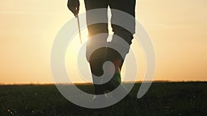 farmer in boots walks the farm close-up at sunset with a tablet in his hands, the concept of work in agriculture, the