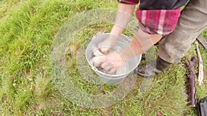 Farmer in Boots washes his hands in a pail standing on green grass