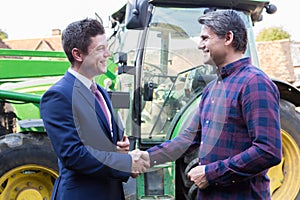 Farmer And Businessman Shaking Hands With Tractor In Background