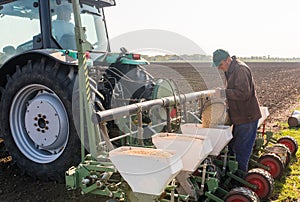 Farmer with can pouring soy seed for sowing crops at agricultural field in spring