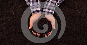 The farmer carefully crushes the fertile black soil in his hands, enjoying its softness. The farmer's hands hold a