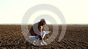 A farmer checks quality of the soil before sowing. woman farmer with a tablet in field holds earth in his hands. girl