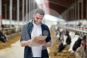 Farmer with clipboard and cows in cowshed on farm