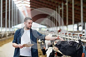 Farmer with clipboard and cows in cowshed on farm