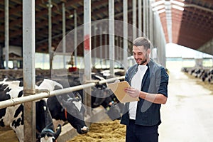 Farmer with clipboard and cows in cowshed on farm