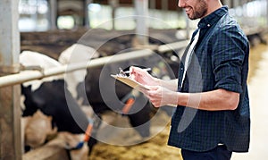 Farmer with clipboard and cows in cowshed on farm photo